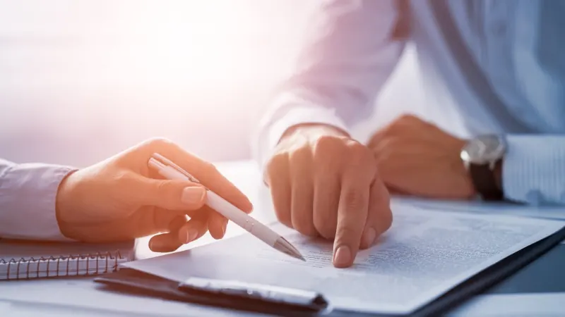 A manager's hands pointing to a line on a printed form beside a notebook.