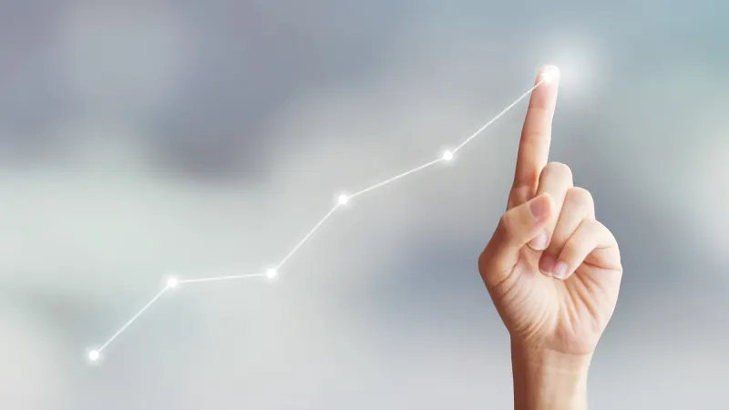 A fingertip tracing a rising line graph against a soft grey background.